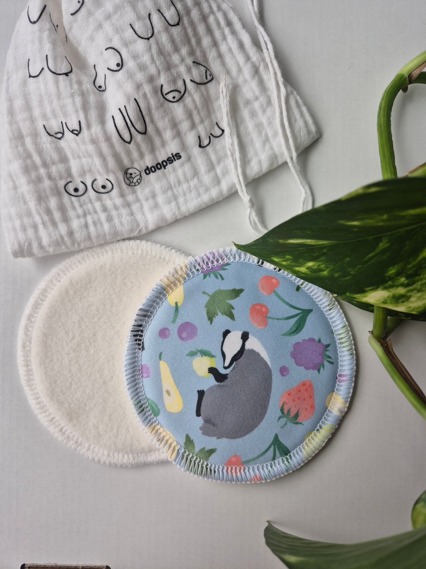 Breast pads with a floral design and badger illustration, alongside a patterned cloth, on a light surface.