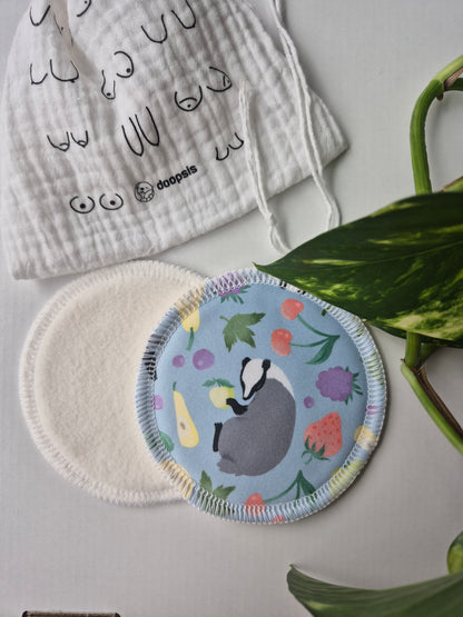 Breast pads with a floral design and badger illustration, alongside a patterned cloth, on a light surface.