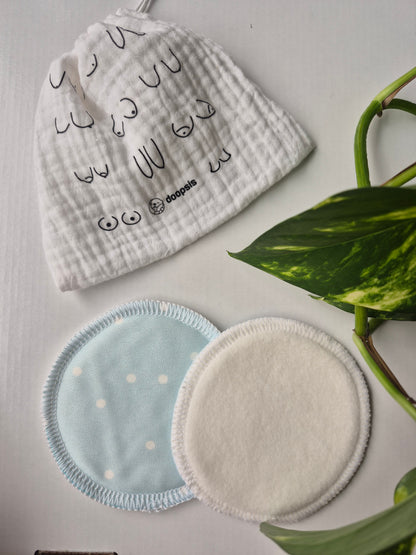 Two nursing pads, one with a pattern and one plain, on a light surface with green leaves in the background.