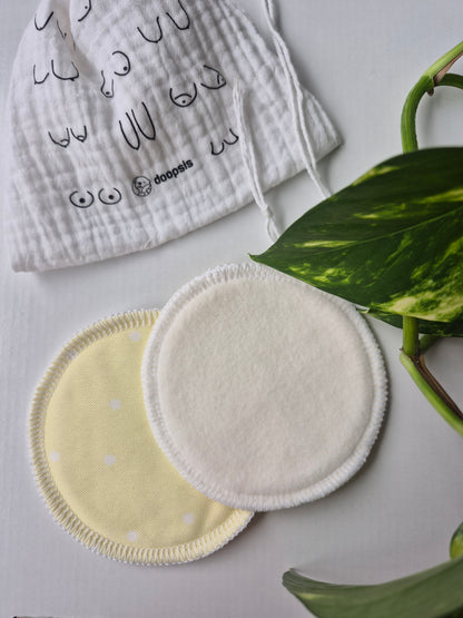 Two reusable breast pads on a white surface with a plant in the background