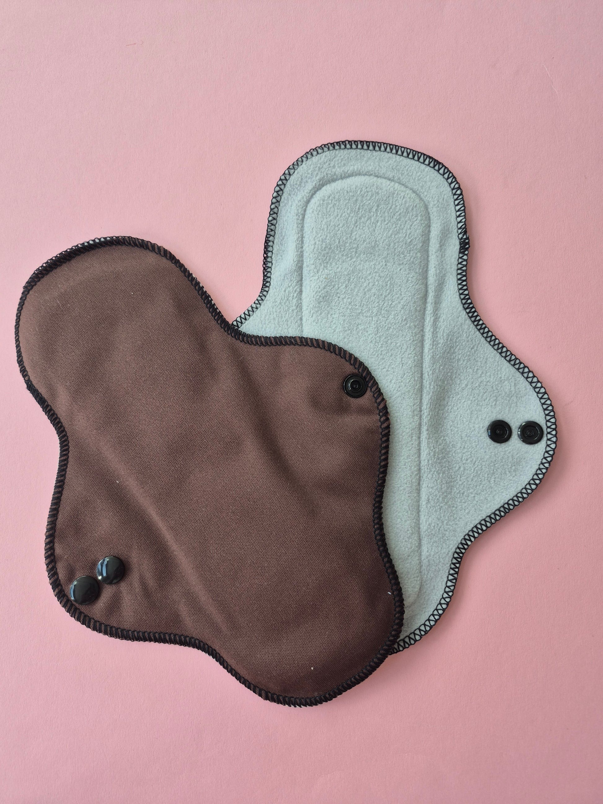 Two menstrual pads, one gray and one brown, on a pink background