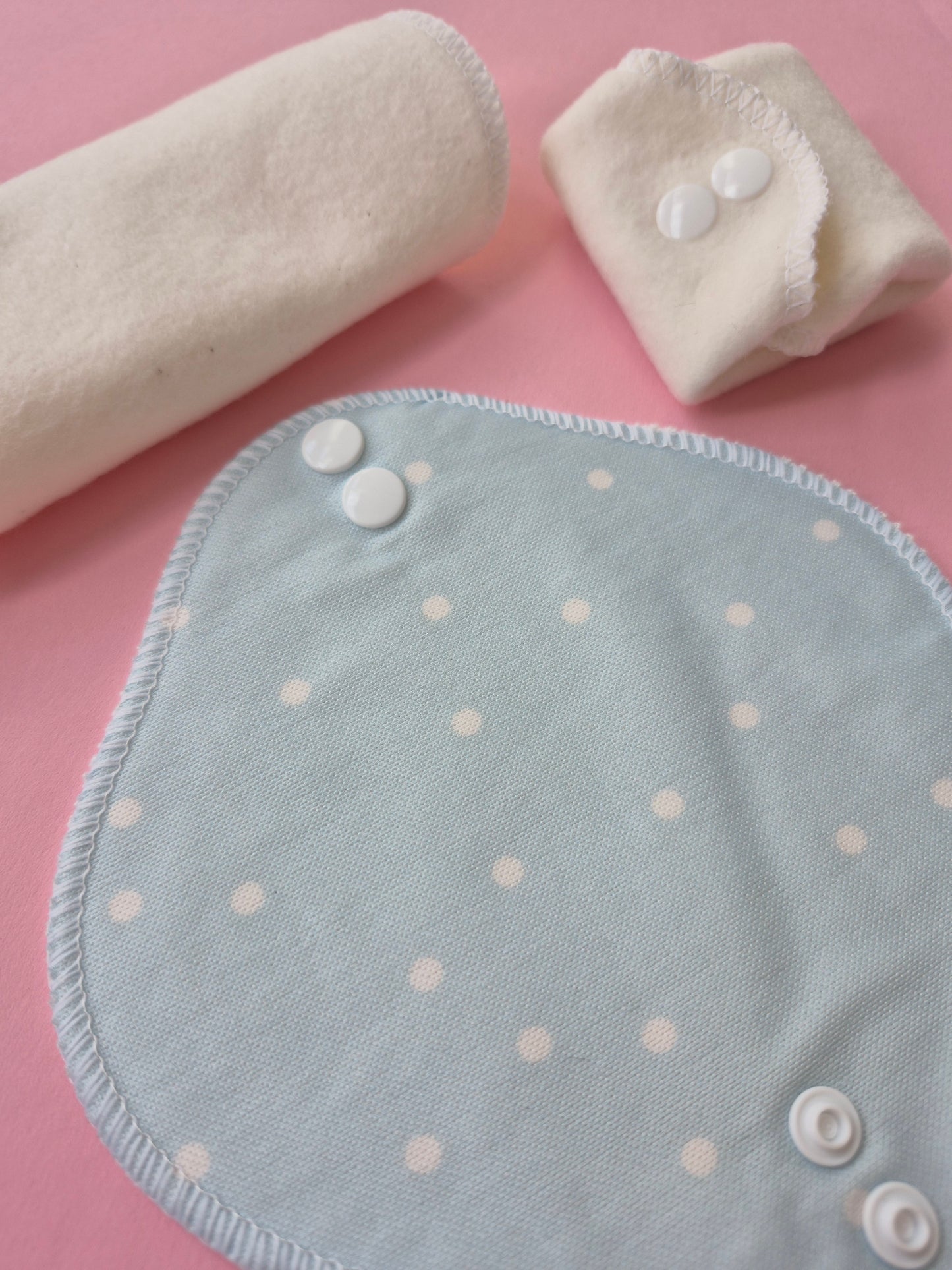 Light blue panty liners with white polka dots and buttons on a pink background
